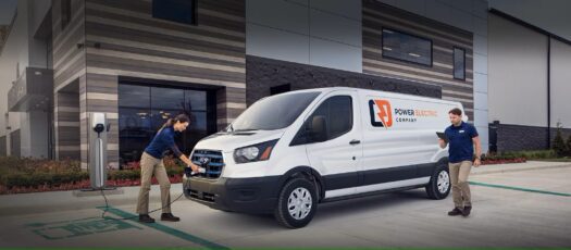 Outside of a Ford E-transit van with a woman plugging into an electric charger.